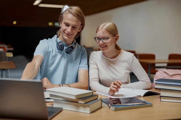 Deux étudiants talentueux travaillant ensemble sur un projet universitaire assis dans une bibliothèque