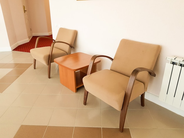 Deux fauteuils marron et une table basse entre eux contre un mur rose, un intérieur moderne d'un salon ou d'un hall d'hôtel.