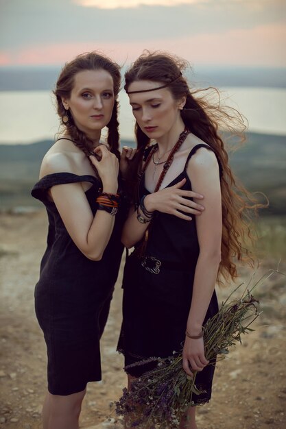 Deux Femme En Robes Noires Marchent Sur La Montagne Avec Un Bouquet De Fleurs En été Au Coucher Du Soleil