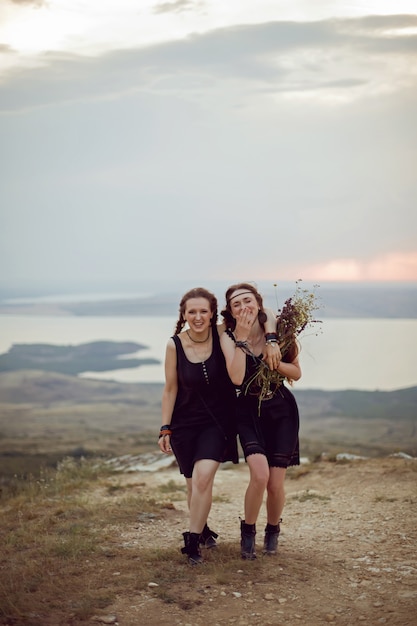 Deux femme en robes noires marchent sur la montagne avec un bouquet de fleurs en été au coucher du soleil