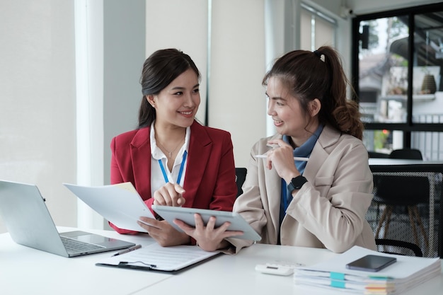 Deux femmes d'affaires asiatiques heureuses parlant et consultant travaillant ensemble au bureau