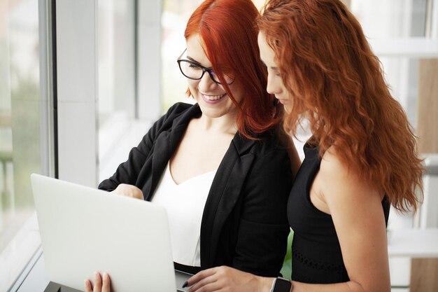 Deux femmes d'affaires aux cheveux roux dans un espace de coworking avec un ordinateur portable sur le bureau au bureau