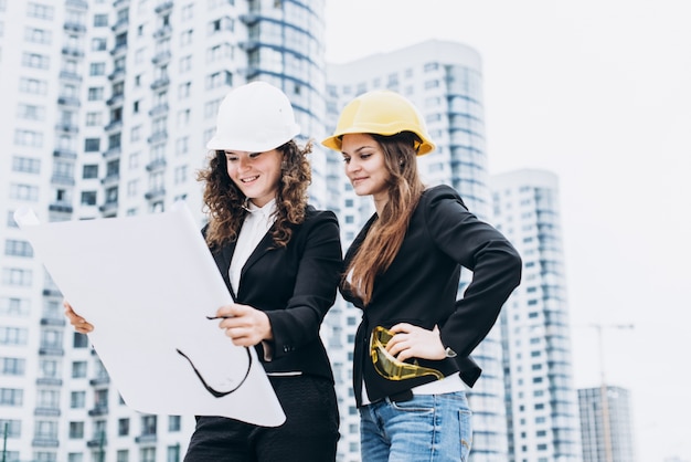 Deux femmes d&#39;affaires dans des casques de protection et des lunettes de sécurité à la recherche de schémas de construction, concept architectural