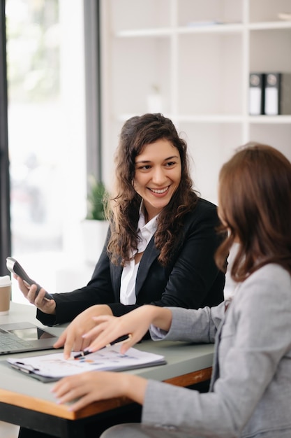 Deux femmes d'affaires discutent de la stratégie de travail et de planification d'un projet d'investissement avec une tablette et un ordinateur portable dans un bureau.