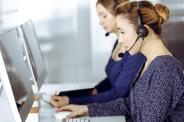 Deux femmes d'affaires ont des conversations avec les clients par casques, tout en étant assises au bureau dans un bureau moderne. Groupe de personnes diverses dans un centre d'appels. Télémarketing et service à la clientèle.