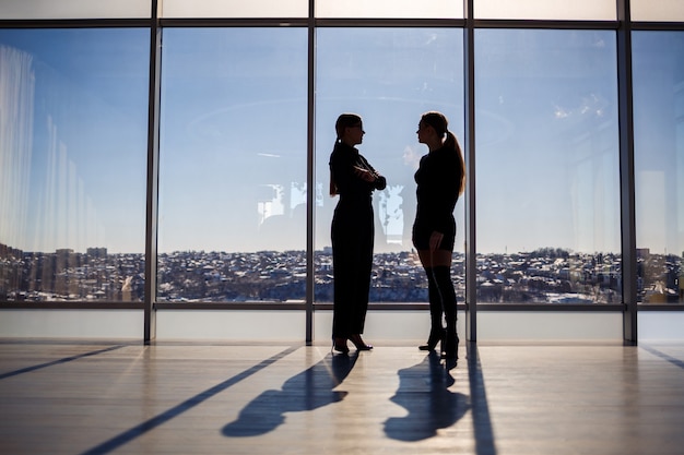 Deux femmes d'affaires profitant de la vue sur la ville et parlant tout en se tenant près de la grande fenêtre du bureau