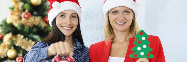 Deux femmes d'affaires souriantes en chapeaux de père Noël tenant un réveil sur fond de Noël