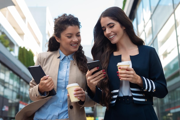 Deux femmes d'affaires tenant une tasse de café et regardant le téléphone