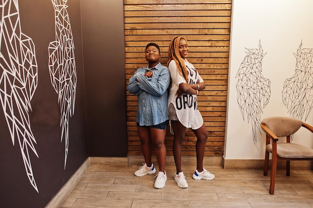 Deux femmes africaines dans des vêtements décontractés élégants posant contre le mur des ailes d'ange