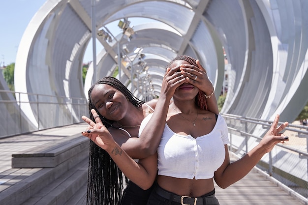 Deux femmes afro-américaines couvrant ses yeux et étreignant par derrière Deux filles surprises Femmes s'amusant et montrant les émotions du visage