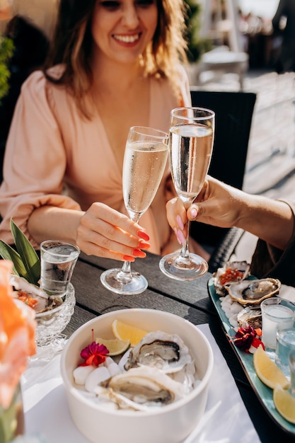 Deux femmes amies mangeant des huîtres fraîches et buvant du prosecco frais au coucher du soleil d'été au restaurant