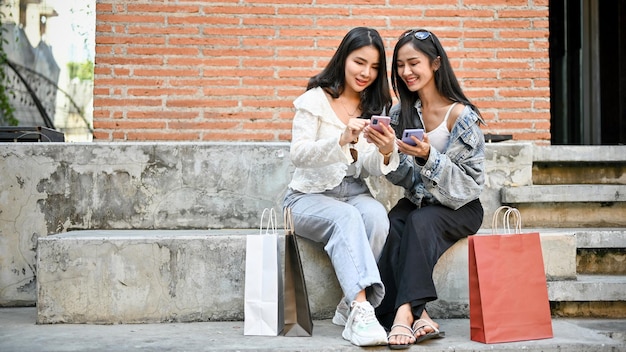 Deux femmes asiatiques assises dans des escaliers à l'extérieur du centre commercial regardant l'écran de leur smartphone