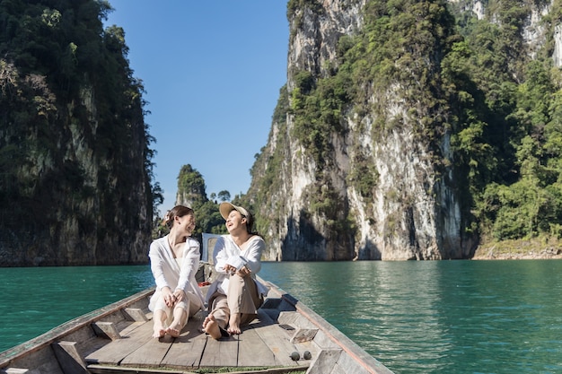 Photo deux femmes asiatiques en chemises blanches sont assises devant un bateau avec une belle montagne au milieu de la mer lors d'un voyage en thaïlande. incroyable thailande.