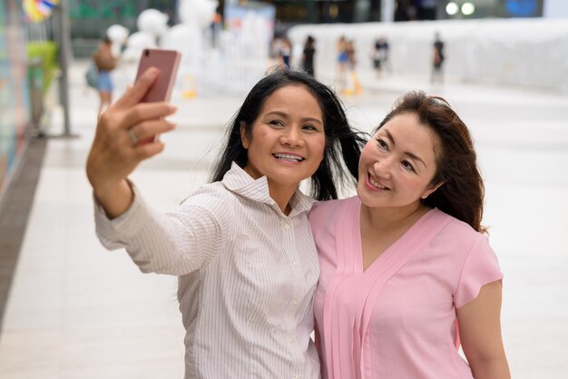 Deux femmes asiatiques matures ensemble à l'extérieur du centre commercial de la ville de Bangkok