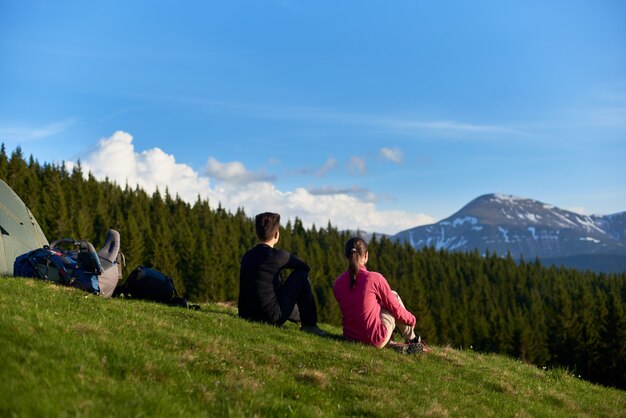 Deux femmes assises au sommet d'une colline près de leur tente bénéficiant d'une vue magnifique sur les montagnes