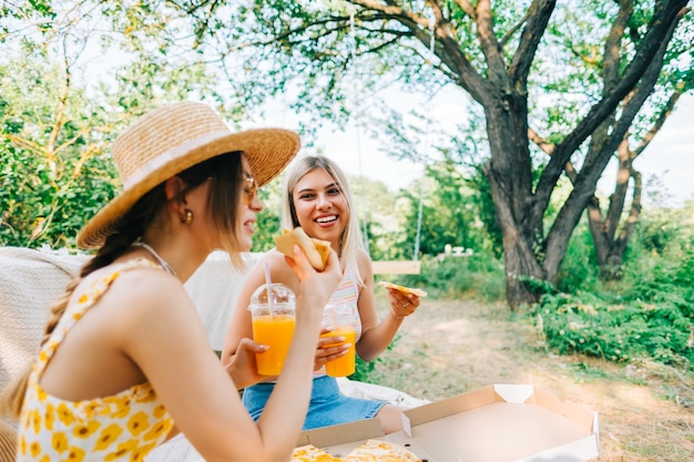 Deux femmes assises sur un canapé dans l'arrière-cour et mangeant des pizzas, buvant de la limonade par une journée ensoleillée d'été.