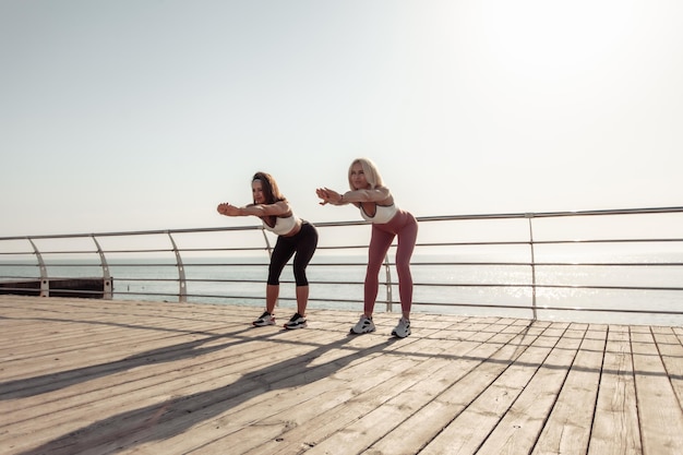 Deux femmes athlétiques s'échauffent en faisant des exercices tôt le matin sur la plage