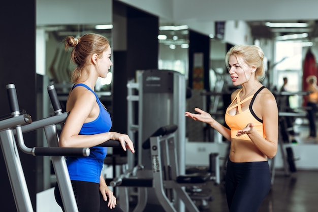 Deux femmes blondes athlétiques parlant dans une salle de sport, une fille communique avec un entraîneur