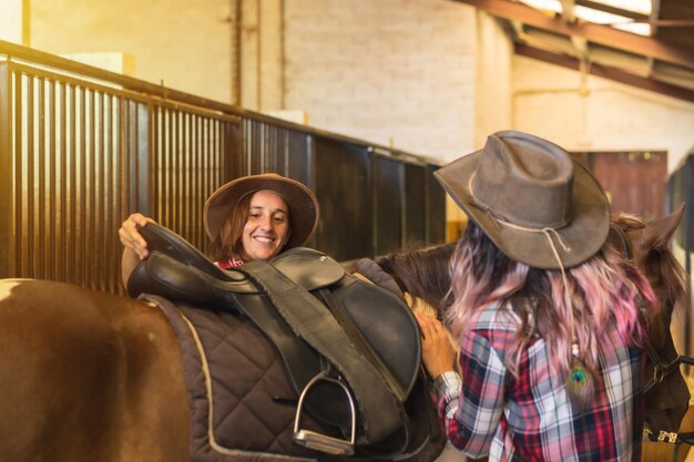 Deux femmes cowgirl se préparent à monter à cheval dans une écurie, des chapeaux et des jeans du sud des États-Unis, photo verticale