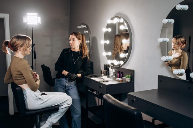 Deux femmes dans un salon de beauté avec des lumières allumées et un miroir au mur