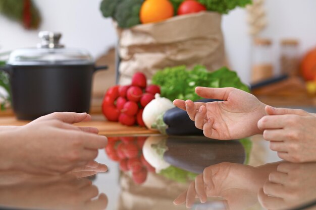 Deux femmes discutant d'un nouveau menu dans la cuisine, en gros plan. Mains humaines de deux personnes gesticulant à la table parmi les légumes frais. Concept de cuisine et d'amitié.