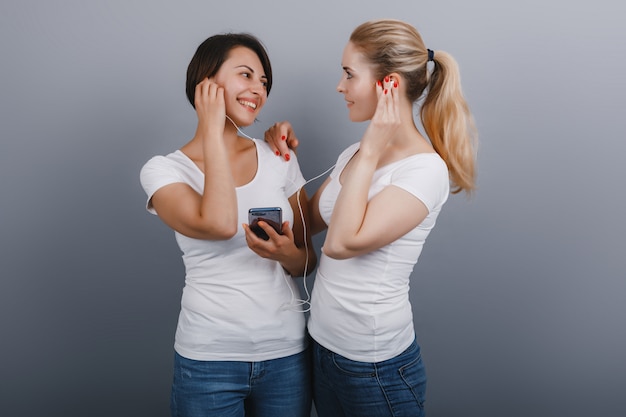 Deux femmes écoutent une musique dans un écouteur se connectant à un smartphone et se regardant