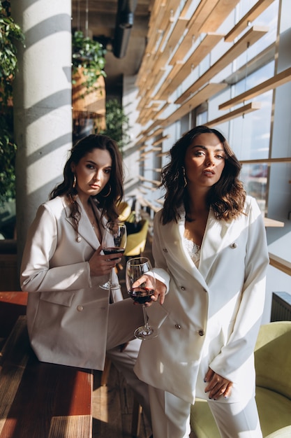 Deux femmes élégantes, sexy et glamour, portent des costumes blancs dans un restaurant avec un verre de vin.