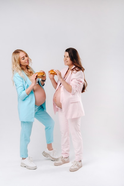 Deux femmes enceintes en costume avec des hamburgers à la main sur fond gris