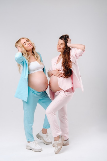 Deux femmes enceintes avec de gros ventres en costume sur fond gris.