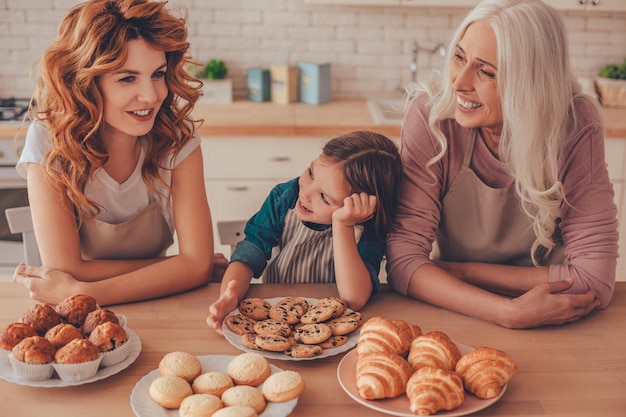 Deux femmes et un enfant avec des produits de boulangerie sur la table riant de la cuisine