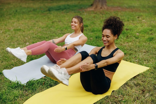 Deux femmes de fitness souriantes s'entraînent sur un tapis de yoga sur l'herbe en plein air concept de vie saine