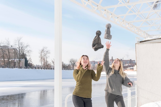 deux femmes jettent leur chapeau debout sur la rive d'une rivière gelée en hiver