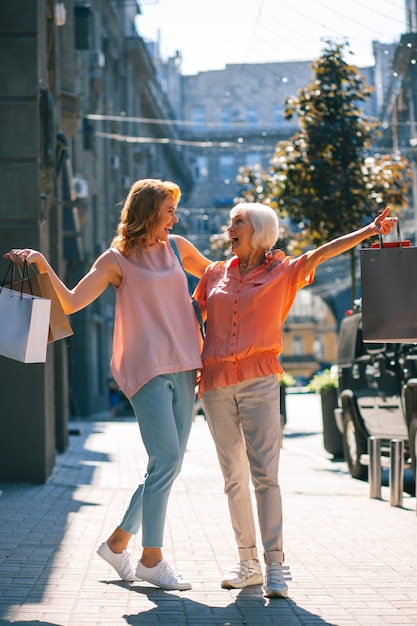 Deux femmes joyeuses se souriant dans la rue avec des sacs à provisions dans les mains