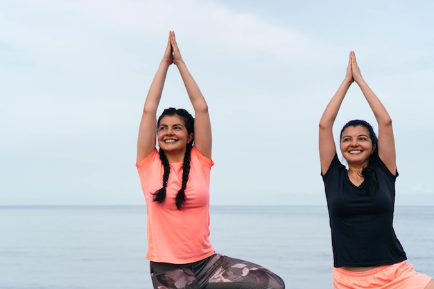 Deux femmes latines pratiquant le yoga, s'étirant sur la plage.