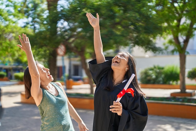 Photo deux femmes mère et fille jetant un chapeau gradué au ciel au parc