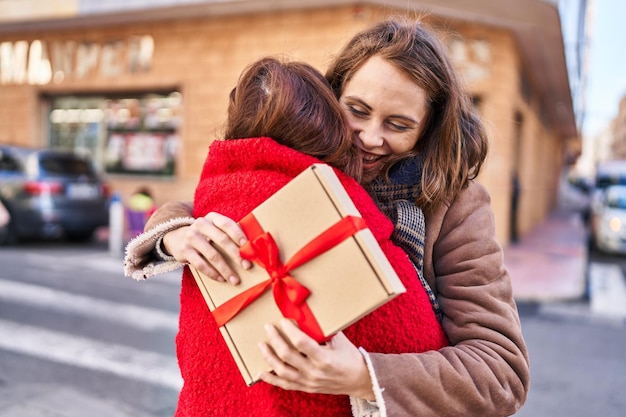 Deux femmes mère et fille se serrant dans leurs bras surprise avec un cadeau dans la rue