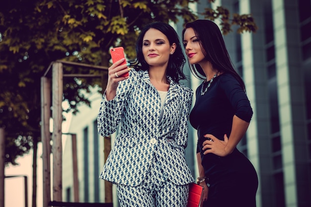 Deux femmes à la mode dans des vêtements élégants et des lunettes de soleil posant dans un quartier urbain d'affaires.