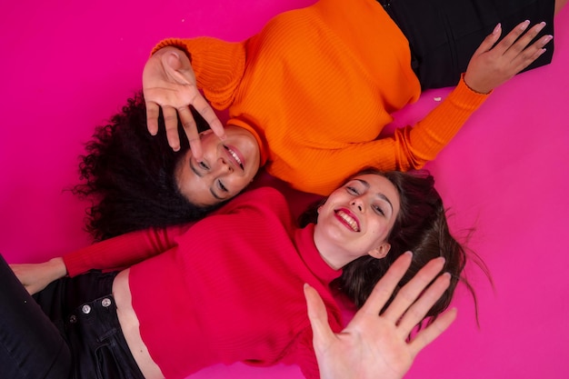 Deux femmes multiethniques allongées souriantes dans un style de vie à la mode posant sur fond rose