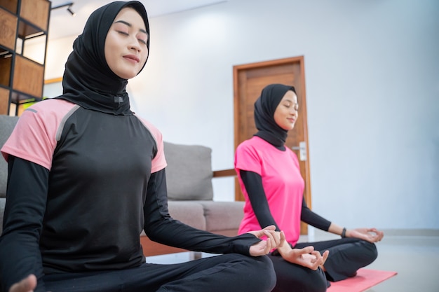 Deux femmes portant un foulard souriant tout en faisant des mouvements brusques tout en faisant de l'exercice à l'intérieur