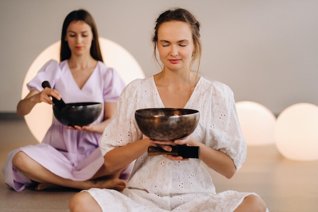 Deux femmes professeurs de yoga jouant un bol tibétain dans la salle de sport lors d'une retraite de yoga