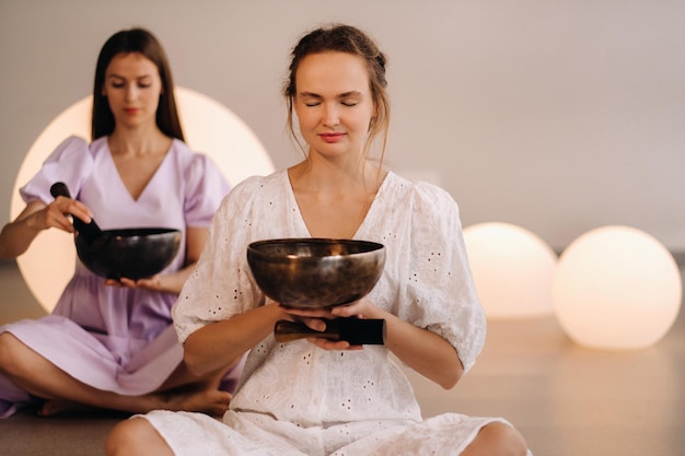 Deux femmes professeurs de yoga jouant un bol tibétain dans la salle de sport lors d'une retraite de yoga