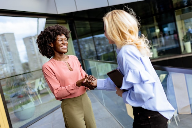 Deux femmes professionnelles partageant une conversation joyeuse dans un immeuble de bureaux moderne à IA générative