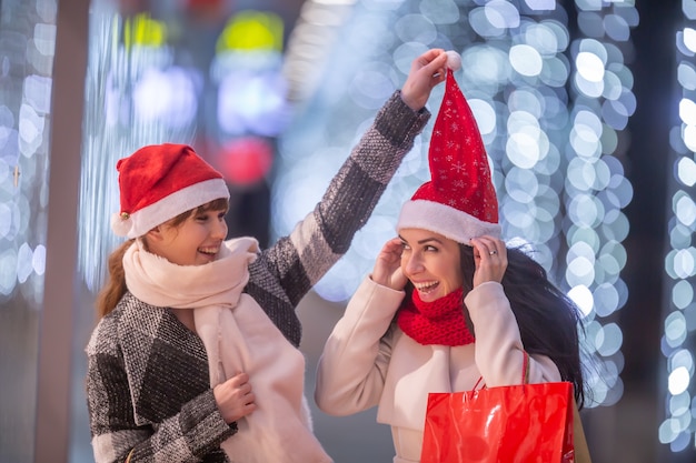 Deux femmes s'amusant avec des chapeaux de Noël en faisant leurs courses à l'extérieur du centre commercial.