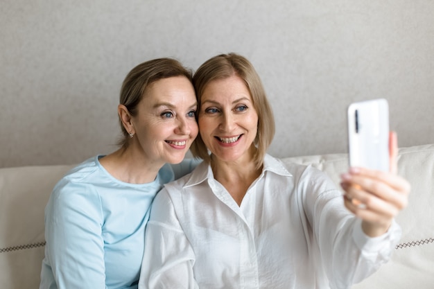 Deux femmes s'assoient sur le canapé et prennent un selfie au téléphone tout en parlant