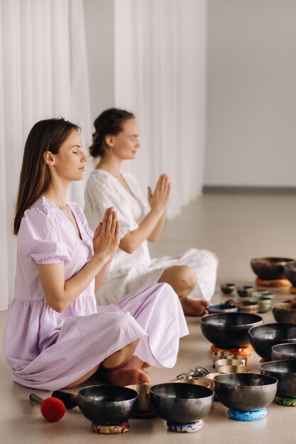 Deux femmes sont assises avec des bols tibétains en position du lotus avant un cours de yoga dans la salle de sport