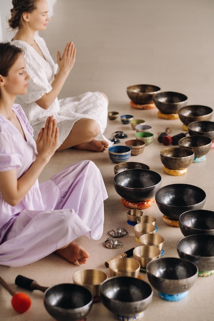 Deux femmes sont assises avec des bols tibétains en position du lotus avant un cours de yoga dans la salle de sport