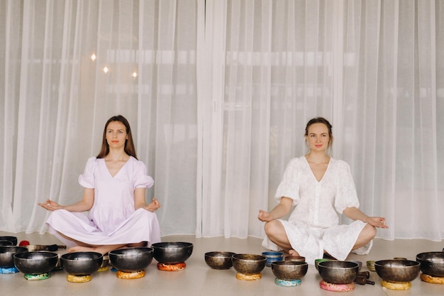 Deux femmes sont assises avec des bols tibétains en position du lotus avant un cours de yoga dans la salle de sport