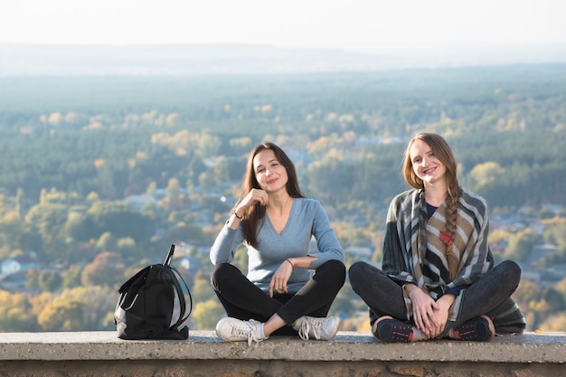 Deux femmes souriantes, assis sur une colline, forêt d'automne au loin