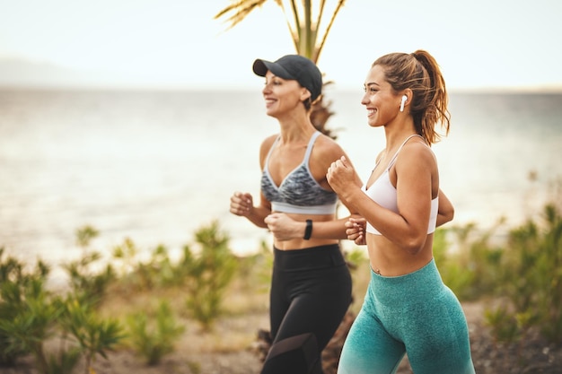 Deux femmes souriantes et heureuses courent le long du chemin au bord de la mer et profitent de la journée ensoleillée d'été.