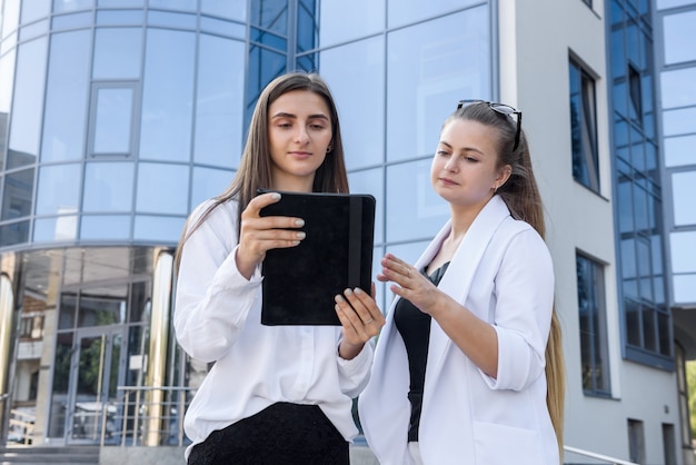 Deux femmes souriantes à la recherche sur tablette à l'extérieur de l'immeuble de bureaux